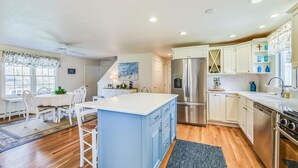 A kitchen with a central island, white cabinetry, stainless steel appliances, and a dining area with a table and chairs. - Comfy Cape Home: Close to Mayflower Beach, golf course, and Downtown  (Dennis)