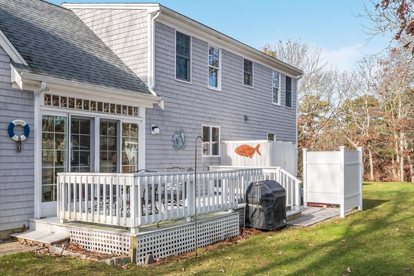 A two-story house with a covered patio, a grill, and a white fence.