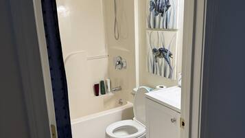 A bathroom with a bathtub, toilet, and shower. There are towels and toiletries on the counter.