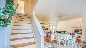 A staircase with wooden steps and white walls, leading to a dining area with a white table and chairs, and a kitchen in the background. - Comfy Cape Home: Close to Mayflower Beach, golf course, and Downtown  (Dennis)