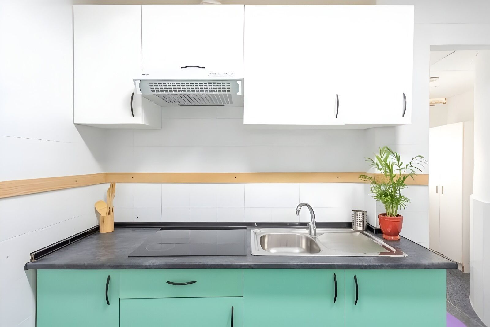 A modern kitchen with white cabinets, a black countertop, a stainless steel sink, and a built-in range hood.