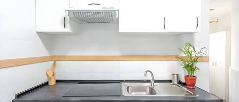 A modern kitchen with white cabinets, a black countertop, a stainless steel sink, and a built-in range hood.