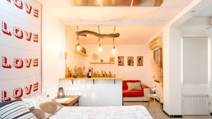Une chambre avec un lit, un canapé rouge, une petite table et un mur sur lequel est écrit le mot « AMOUR ».
