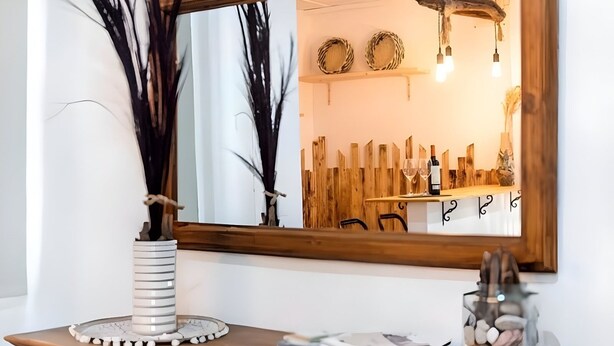 Une commode en bois avec un miroir, un vase à rayures et une petite table sur laquelle se trouvent un livre et un verre d’eau.
