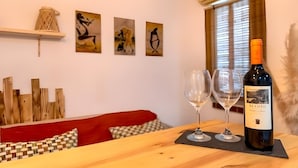 Une table en bois, avec deux verres à vin et une bouteille de vin El Coto. Des tableaux abstraits ornent le mur, et un canapé rouge est installé dans la pièce.