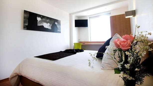 A hotel room with a bed, a painting on the wall, a window, and a flower arrangement. - One Irapuato (Irapuato)