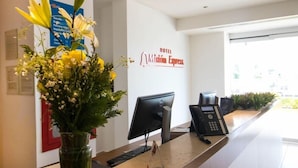 A hotel reception desk with a computer, phone, and a vase of flowers. - One Irapuato (Irapuato)
