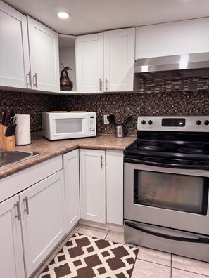 A kitchen with white cabinets, a microwave, a stove, and a patterned rug.