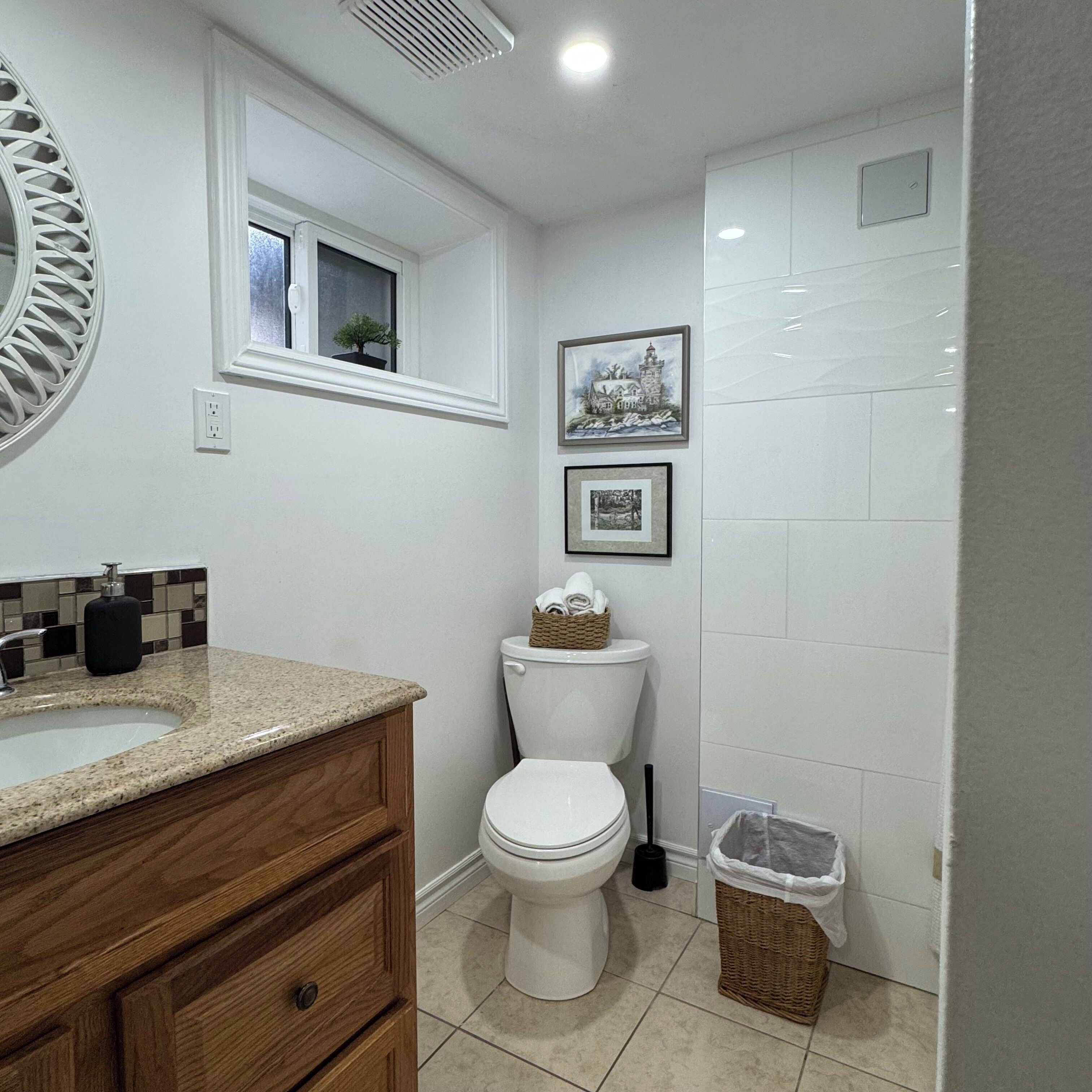 A bathroom with a white toilet, a wooden vanity with a sink, and a mirror. There are two framed pictures on the wall.
