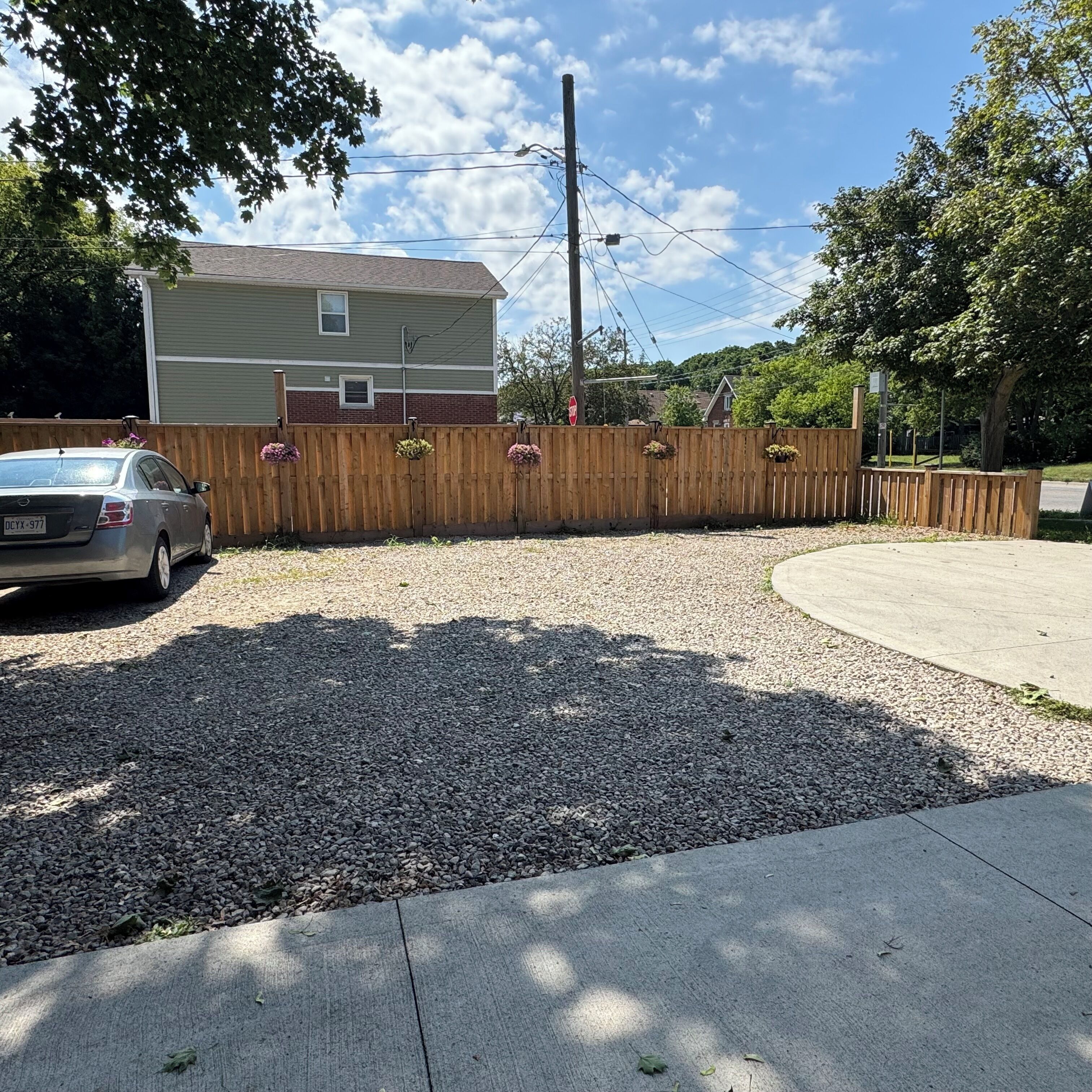 A residential driveway with a gravel surface, a wooden fence, and a parked car.