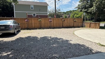 A residential driveway with a gravel surface, a wooden fence, and a parked car.