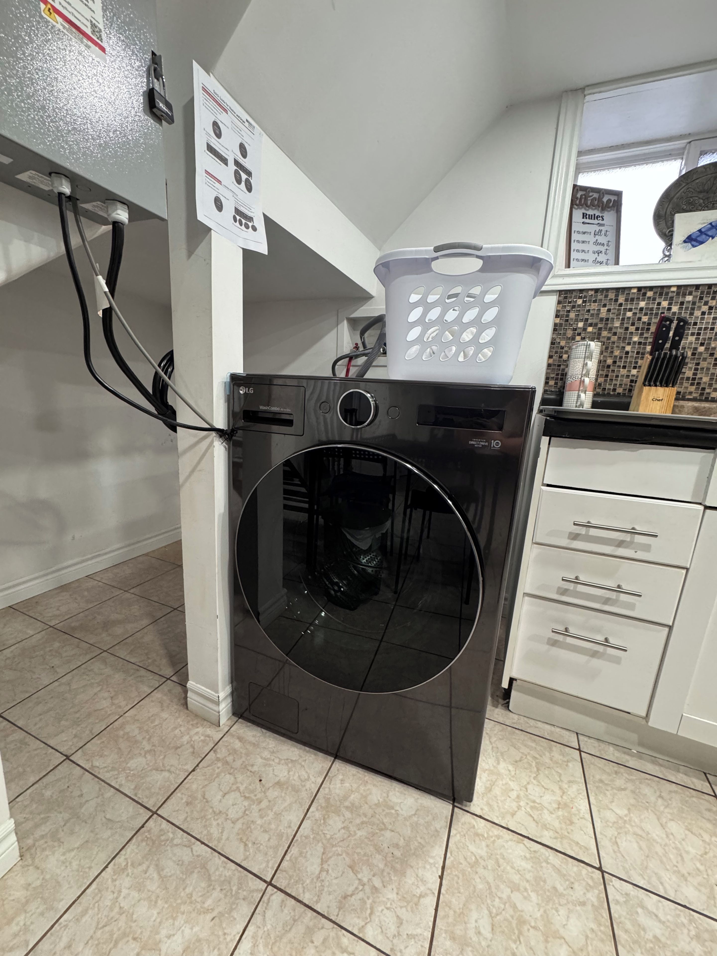 Une cuisine compacte dotée d’un lave-linge et d’un sèche-linge intégrés, d’un plan de travail blanc et d’une fenêtre offrant une vue agréable.