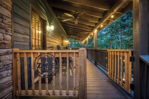 A wooden deck with a railing, a ceiling fan, and string lights.