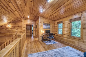 A wooden cabin interior with a desk, computer, and a large window.