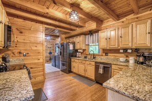 A wooden cabin-style kitchen with granite countertops, a refrigerator, and a coffee maker.