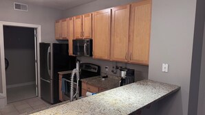 A kitchen with wooden cabinets, a stainless steel refrigerator, a microwave, and a granite countertop.