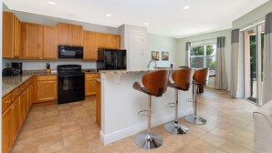 A modern kitchen with wooden cabinets, a central island with bar stools, a built-in microwave, and a stainless steel oven. - Private Villa near Disney world (Kissimmee)