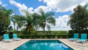 A rectangular pool with two lounge chairs on each side, surrounded by palm trees and hedges. - Private Villa near Disney world (Kissimmee)