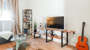 Un soggiorno con un tavolino in vetro, una TV su un mobile in legno, una chitarra e una libreria.