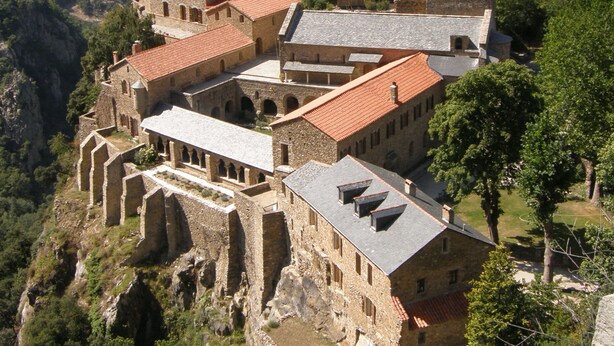 A historic stone building with multiple levels, a central tower, and a courtyard surrounded by trees.