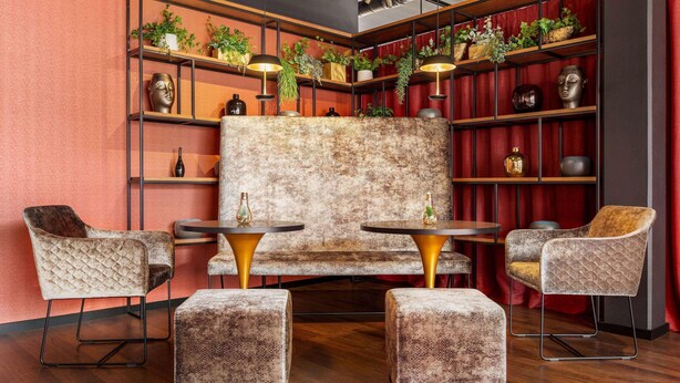 Een zithoek met een gestreept sofa, twee fauteuils en poufs, omringd door planken met planten en decoratieve objecten.