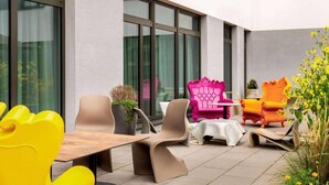 Een buitenzitgedeelte met moderne stoelen en een tafel, grote ramen, en een gevel.