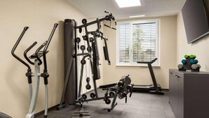 Een sportschool met trainingsapparatuur, een raam met zonwering en een televisie aan de muur.
