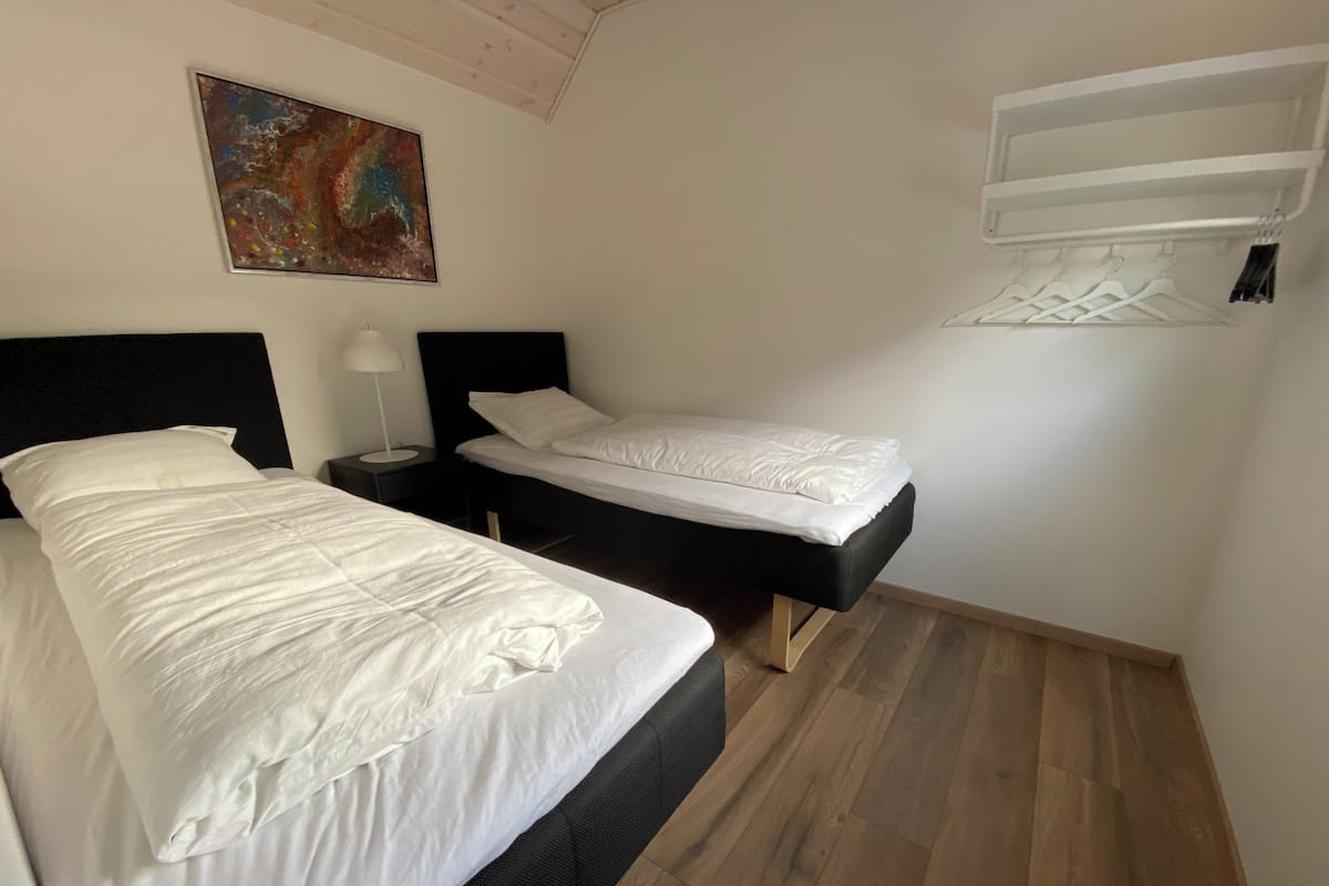 A hotel room with two beds, a nightstand with a lamp, a painting on the wall, and a built-in air conditioning unit.