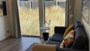 Una sala de estar moderna con un sofá oscuro, una mesita redonda y vistas a un jardín a través de ventanas grandes.