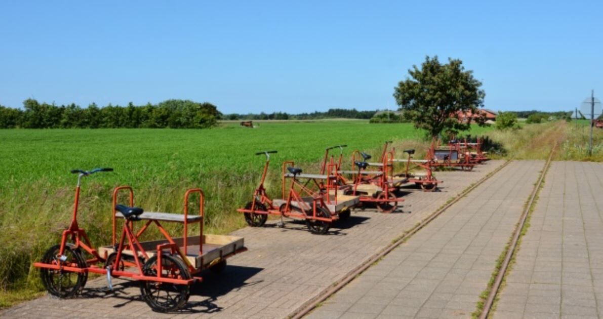 Une rangée de machines agricoles rouges est garée sur un chemin pavé, à côté d’un champ verdoyant.