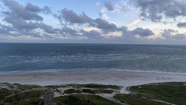 Una playa con una estructura similar a un castillo en primer plano y un cielo despejado con nubes.