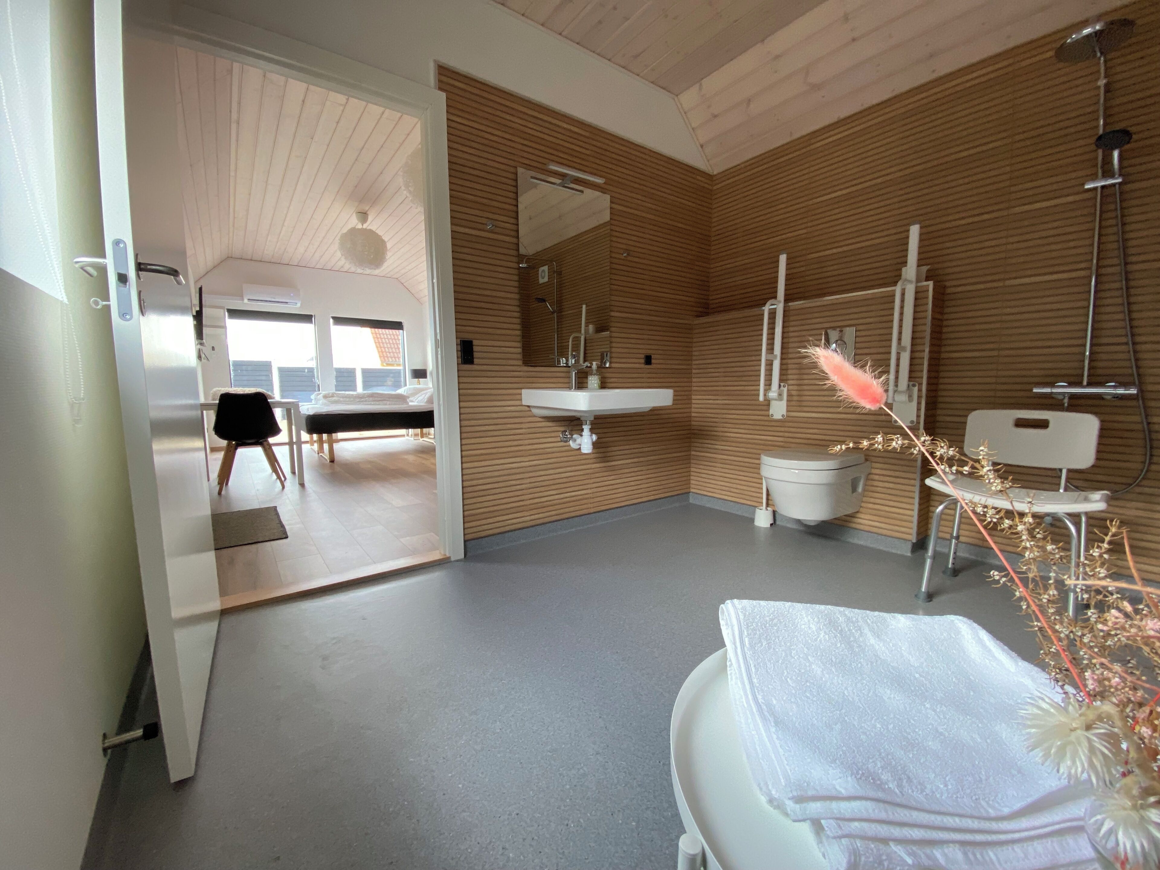 Een moderne badkamer met een houten wand, een wit wastafelmeubel, toilet en douchegedeelte.