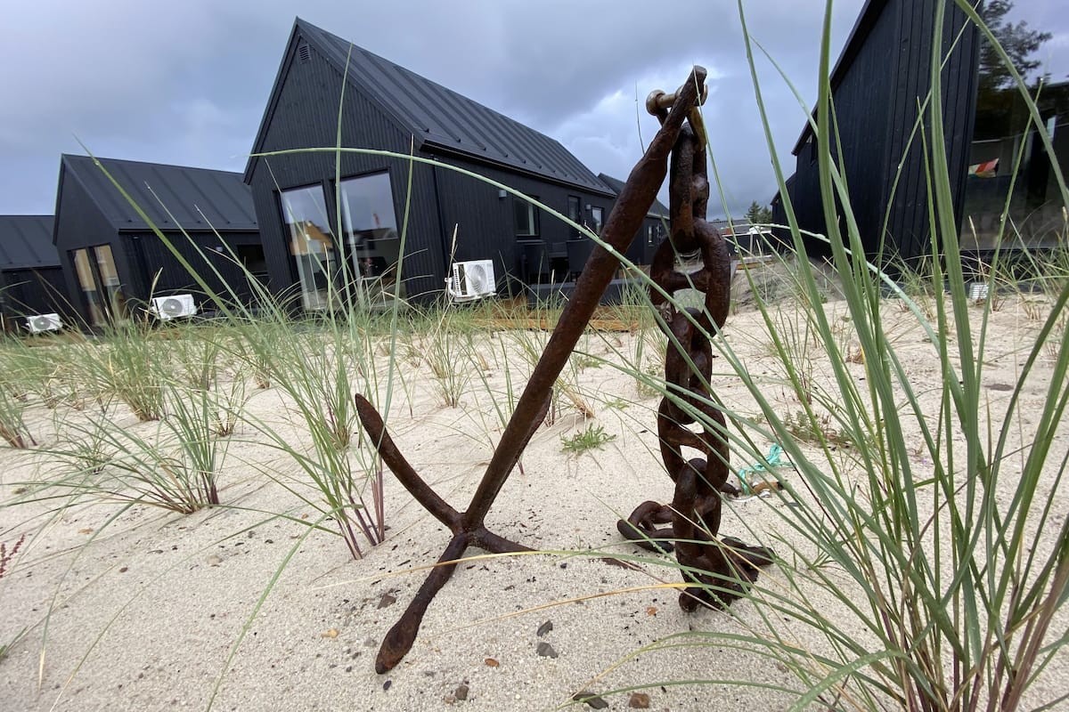 A metal sculpture in a sandy area with buildings in the background.