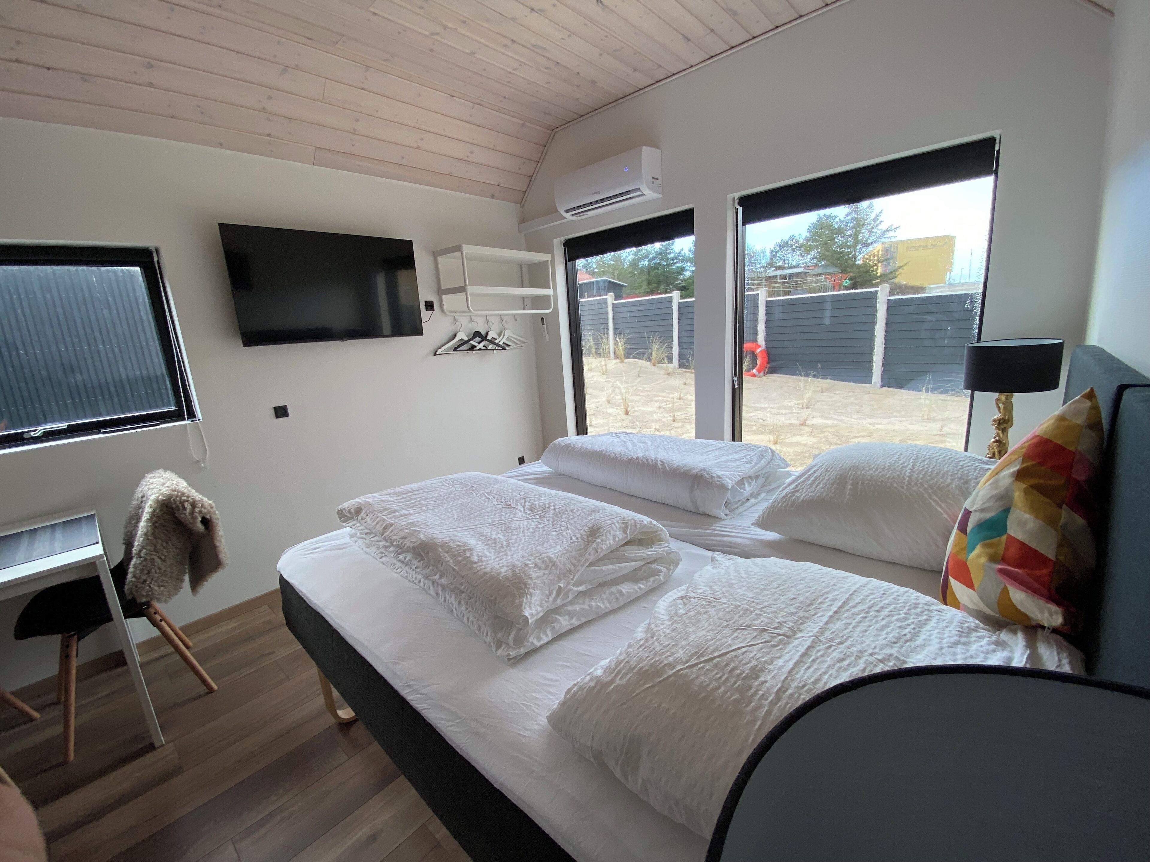 A modern bedroom with a bed, a TV mounted on the wall, and a window with a view of the outside.
