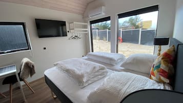A modern bedroom with a bed, a TV mounted on the wall, and a window with a view of the outside.
