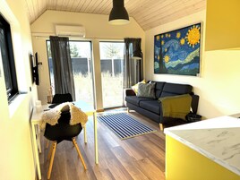 Una sala de estar moderna con un sofá oscuro, una mesita, una silla y un cuadro en la pared.