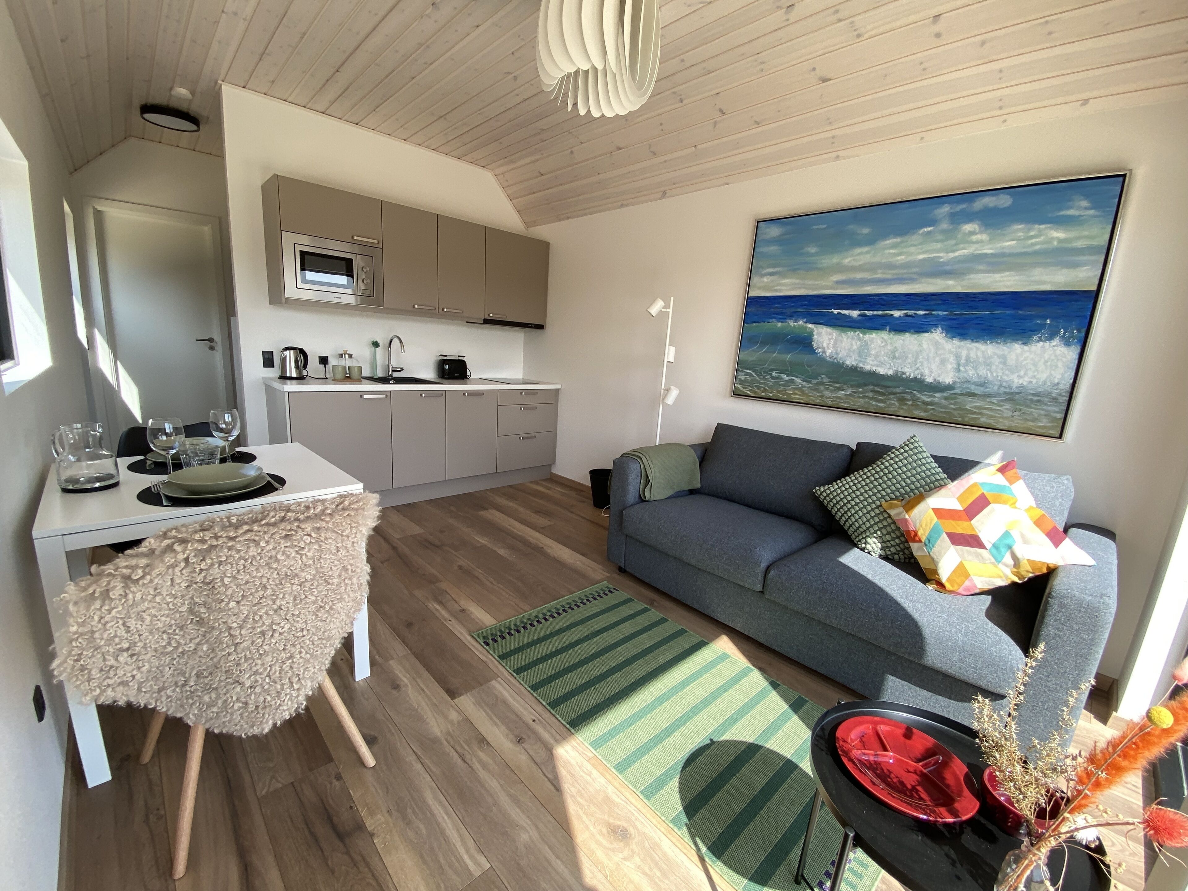 A compact living space with a kitchenette, a dining area, and a sofa with a view of the ocean.