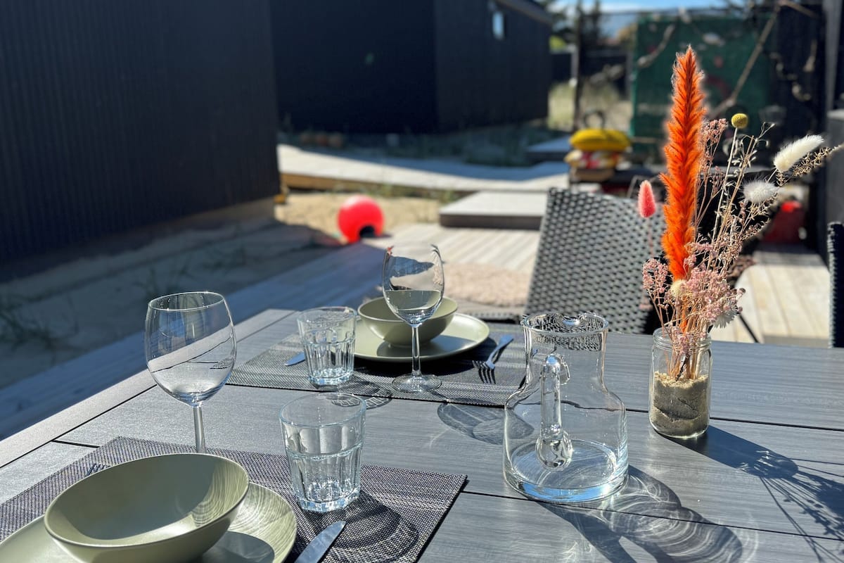 A table set for a meal with clear glassware, plates, and a decorative vase with dried plants.