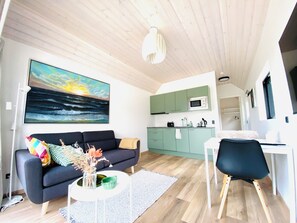 A modern living room with a sofa, coffee table, and artwork. A kitchen is visible in the background with green cabinets and a microwave. - Esehytter Luxury Holiday Home near Beach (Norre Nebel)