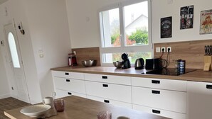 A modern kitchen with white cabinets, a wooden countertop, and a large window providing natural light. - Maison spacieuse avec piscine (Condé-sur-Risle)