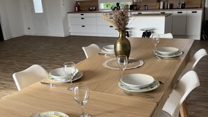 A dining area with a long wooden table set for six, white chairs, and a vase with dried flowers. - Maison spacieuse avec piscine (Condé-sur-Risle)
