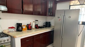 Une cuisine dotée de meubles en bois foncé, d’un réfrigérateur en acier inoxydable, d’une cuisinière à gaz et de divers appareils électroménagers posés sur le plan de travail.