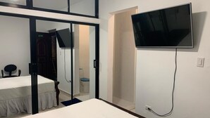 Une chambre à coucher avec un lit, un téléviseur fixé au mur et une porte donnant sur une salle de bain.