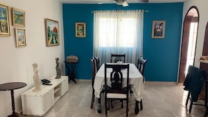 Un coin repas comprenant une table et des chaises, un ventilateur de plafond et une fenêtre avec des rideaux.