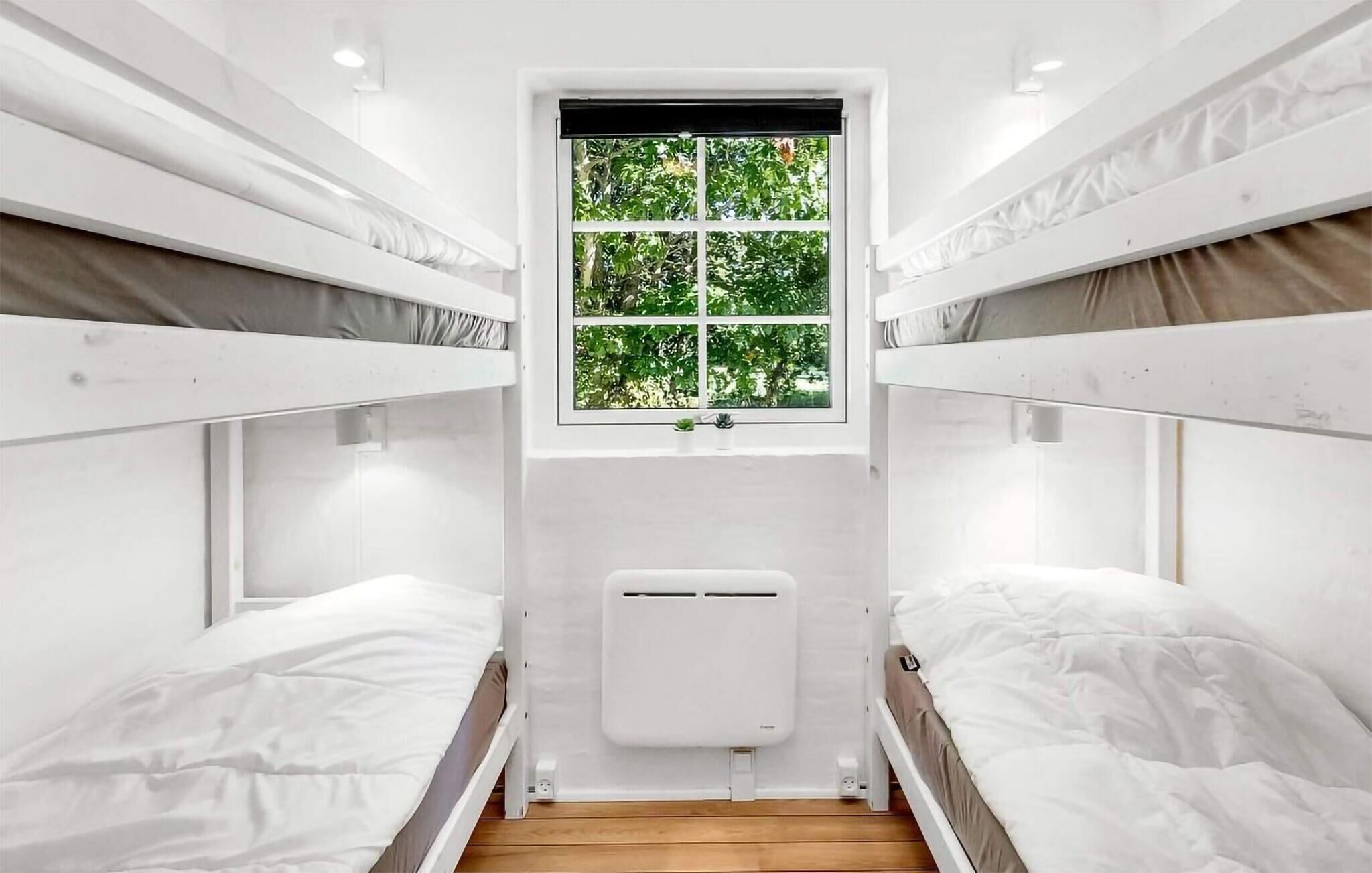 Quarto com beliche, janela, paredes brancas e radiador.