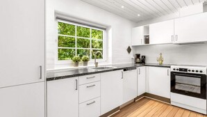 A modern kitchen with white cabinets, a black countertop, a window with a view of greenery, a coffee maker, and an oven. - Stunning home in Ulfborg with sauna (Ulfborg)