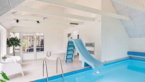 A modern indoor swimming pool with a blue slide, clear glass doors, and a white interior. - Stunning home in Ulfborg with sauna (Ulfborg)