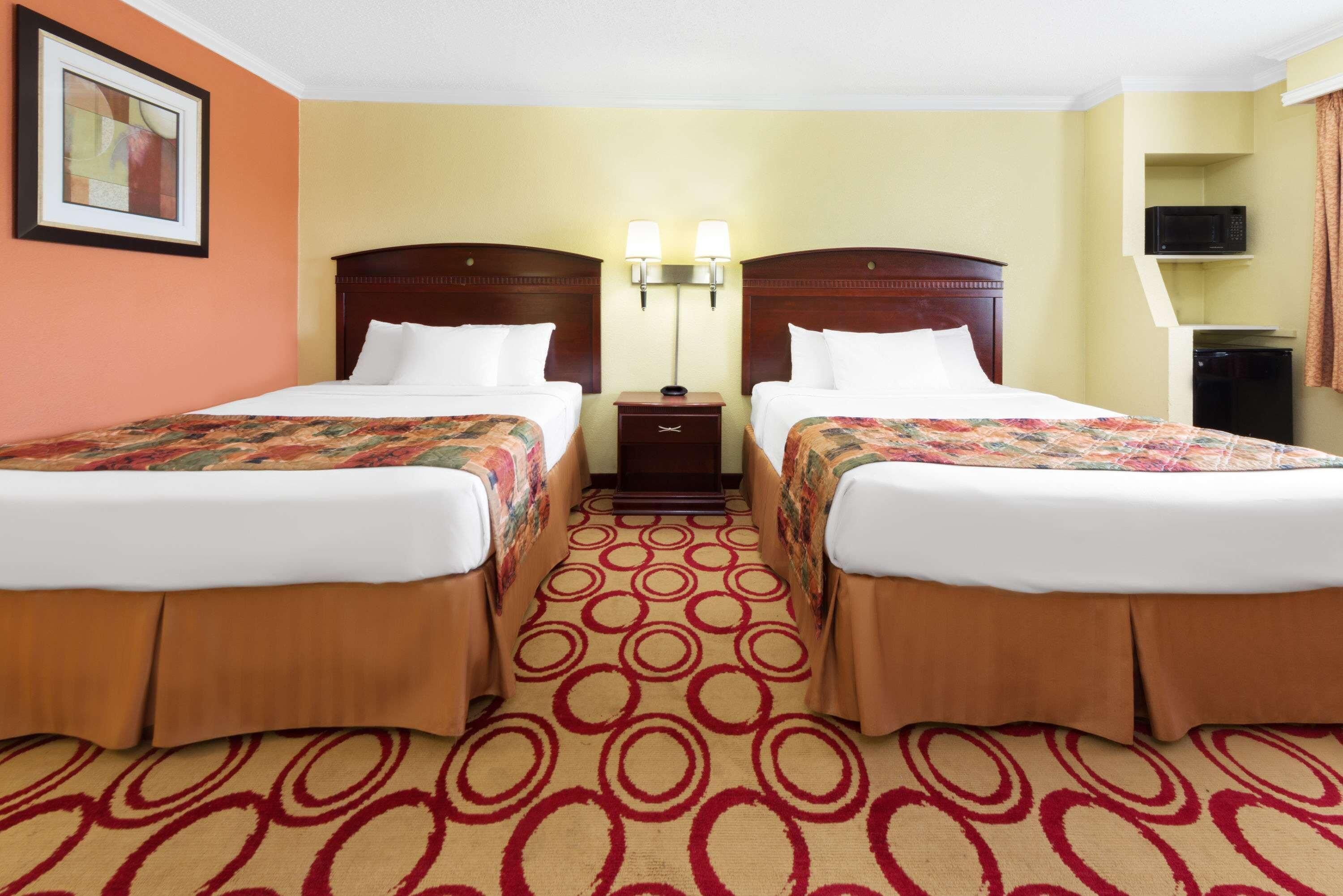 A hotel room with two beds, a nightstand with lamps, a microwave, and a framed picture on the wall.