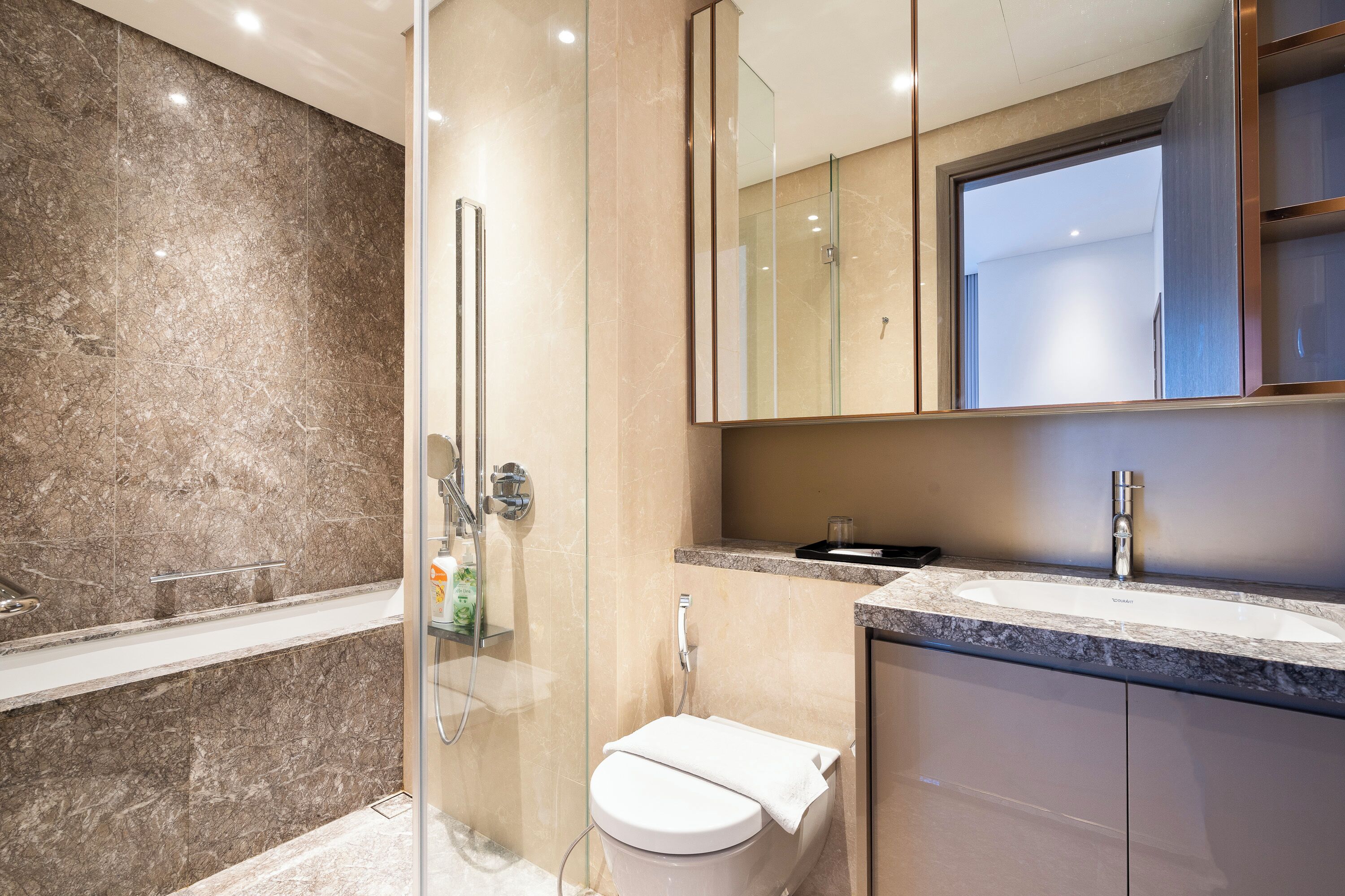 A modern bathroom with a glass-enclosed shower, a white toilet, and a marble-tiled vanity with a sink.