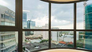 Blick durch ein großes Fenster auf einen Stadtblick mit verschiedenen Gebäuden, darunter das Hotel "NHATHALOPEA HOTEL" und eine Baustelle.